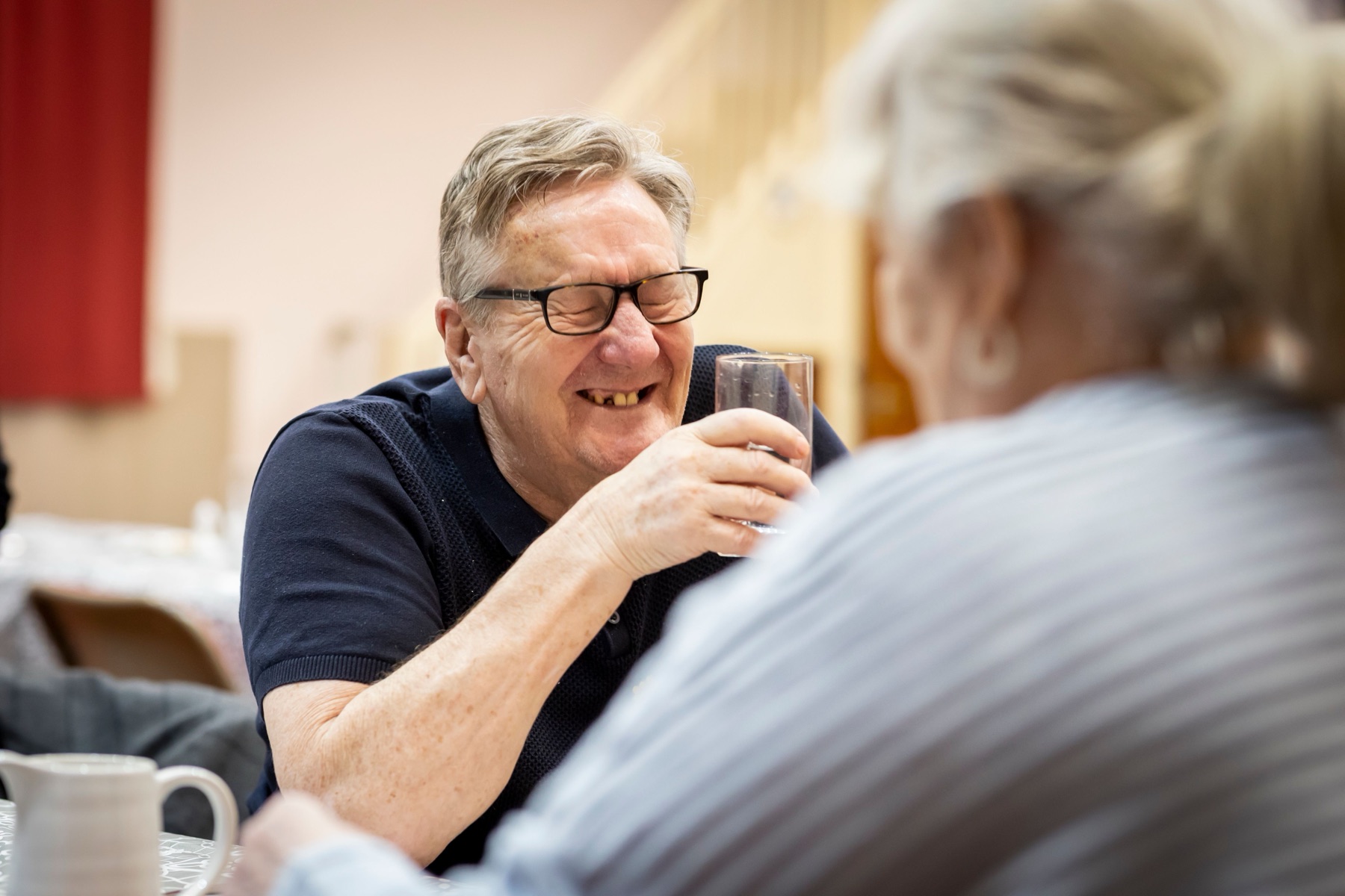 An older man laughing with a companion at a table.