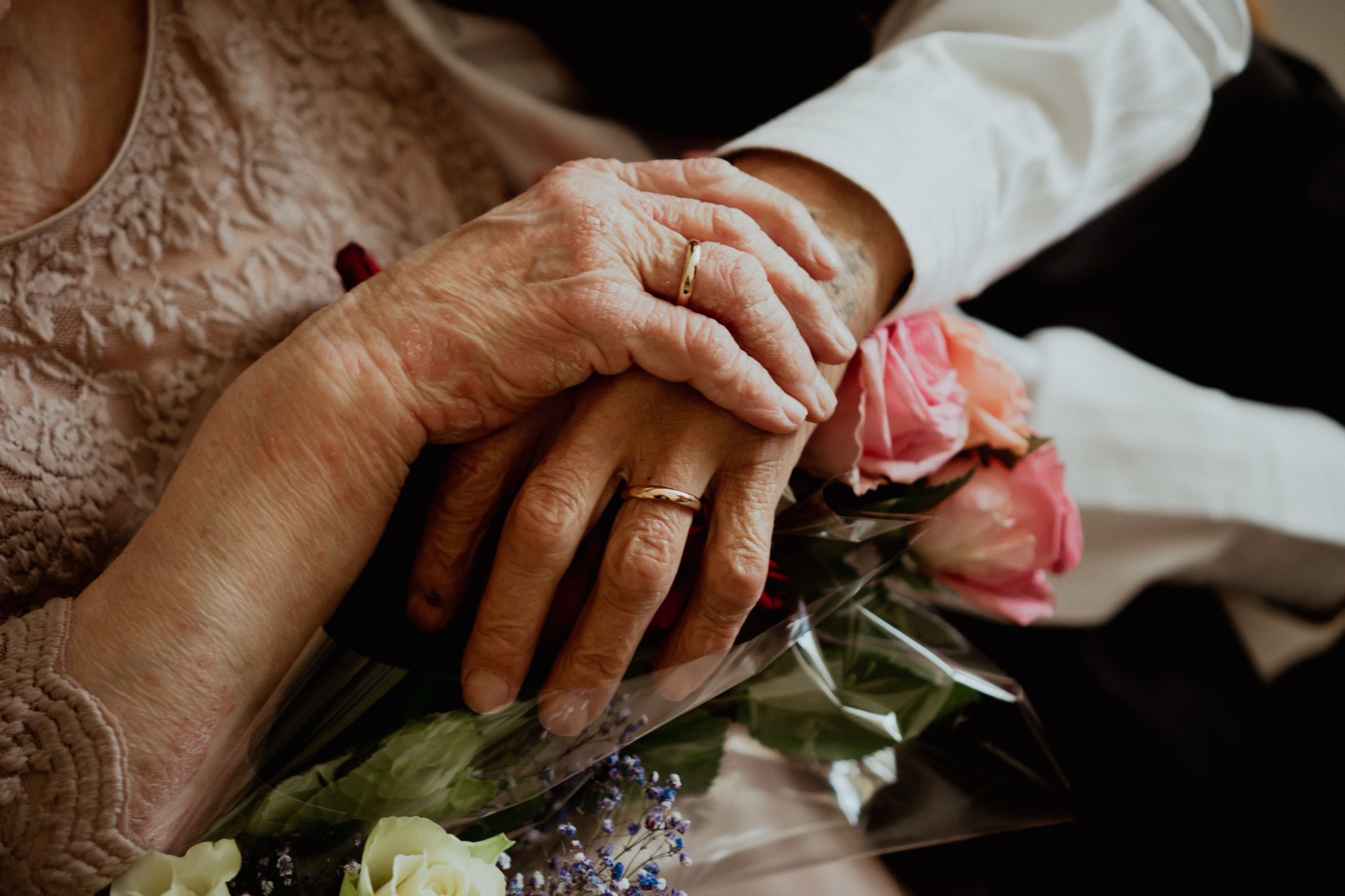 An older person and companion holding hands over a bouquet of flowers.